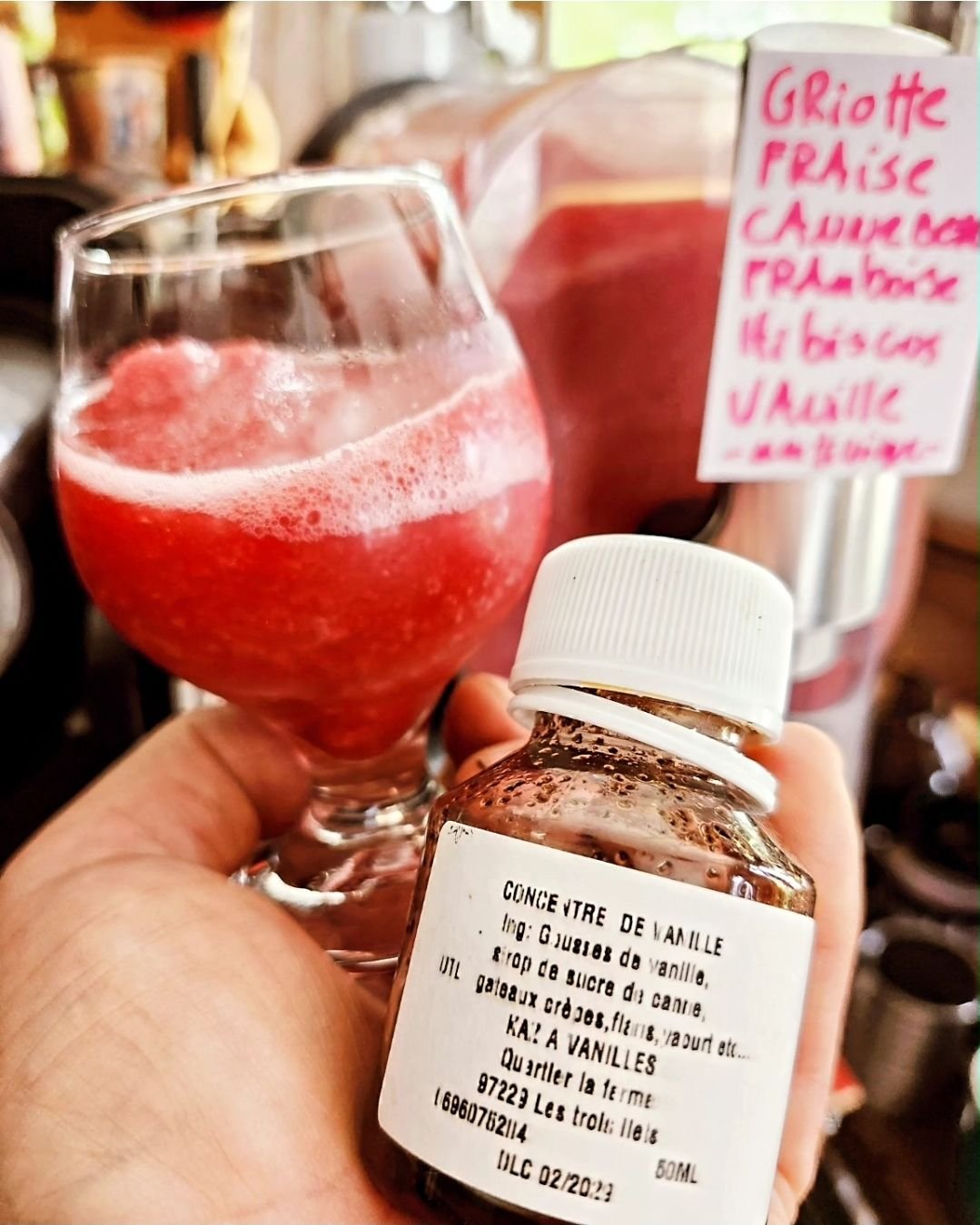 Un verre de kombucha rouge devant l'étiquette manuscrite des parfums du brassin