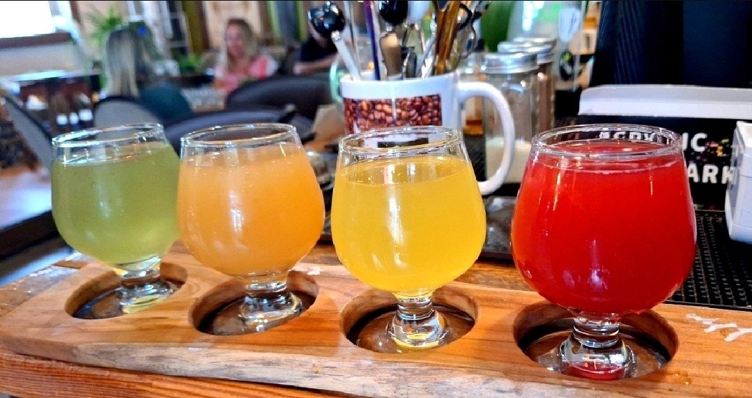 Une planche de dégustation : quatre verres tulipe de kombucha, vert, ambré, jaune et rouge